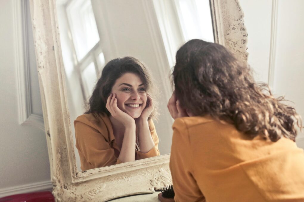 Woman looking in mirror photo by Andrea Piacqua